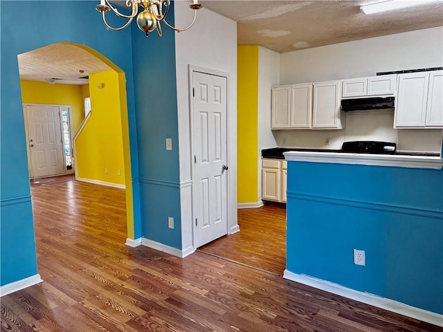 kitchen featuring under cabinet range hood, dark wood-style flooring, white cabinetry, arched walkways, and a notable chandelier