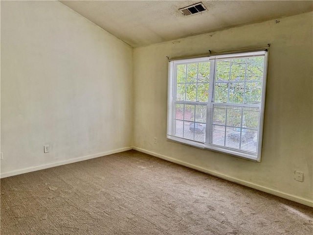 carpeted spare room featuring baseboards, lofted ceiling, and visible vents