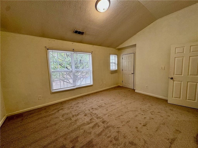 carpeted empty room featuring baseboards, visible vents, a textured ceiling, and vaulted ceiling
