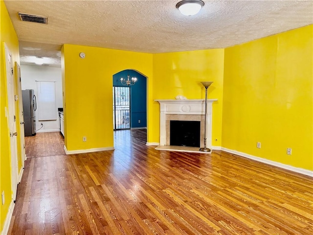 unfurnished living room with wood finished floors, a textured ceiling, arched walkways, a premium fireplace, and baseboards