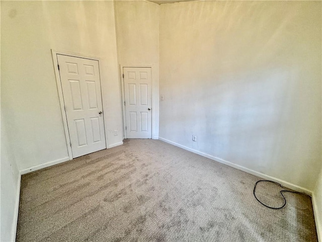 empty room featuring a high ceiling, carpet floors, and baseboards