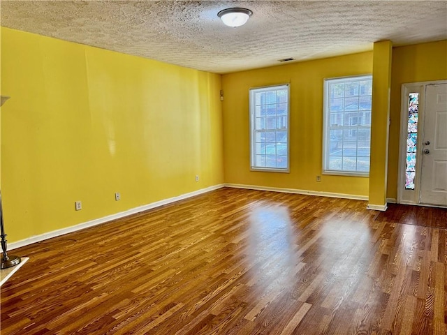 foyer with a textured ceiling, baseboards, visible vents, and wood finished floors