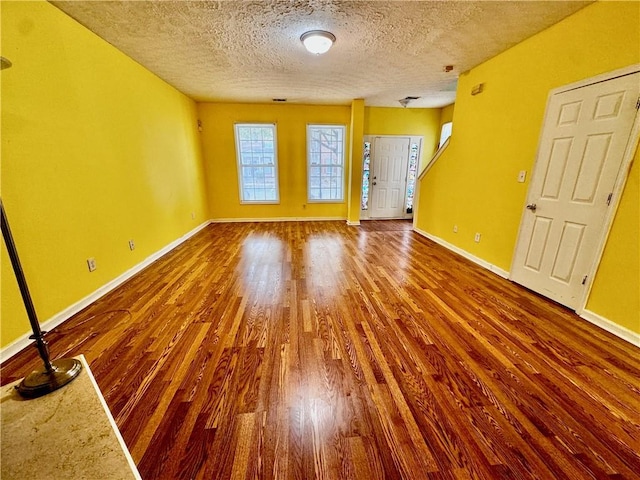 unfurnished living room featuring baseboards, a textured ceiling, and wood finished floors