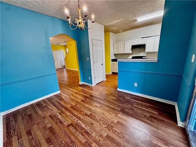 interior space featuring wood finished floors, a notable chandelier, a textured ceiling, baseboards, and arched walkways