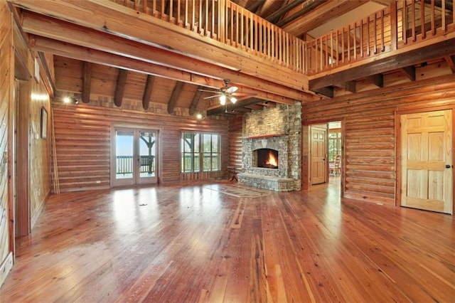 929 Hickory Nut Mountain Rd, Tallulah Falls, GA 30573 - unfurnished living room with a ceiling fan, hardwood / wood-style flooring, a stone fireplace, french doors, and beam ceiling
