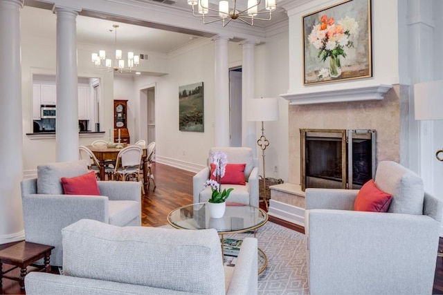 living area featuring an inviting chandelier, crown molding, wood finished floors, baseboards, and ornate columns