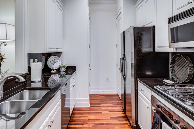 kitchen with a sink, stainless steel appliances, dark stone countertops, and wood finished floors