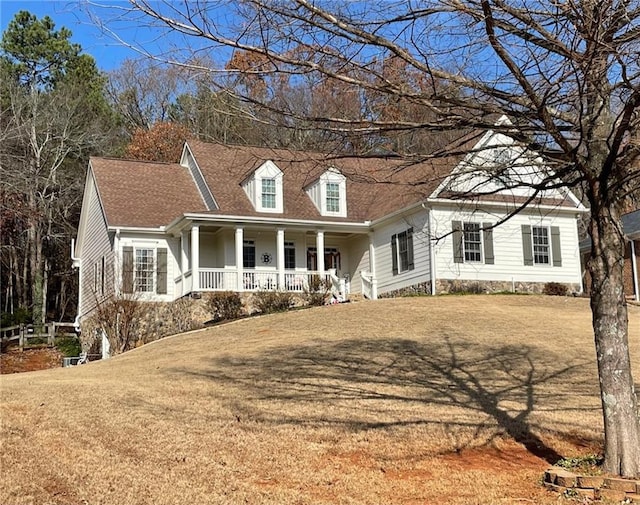 new england style home with roof with shingles, a porch, and a front yard