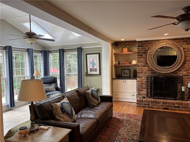 living area with a ceiling fan, a brick fireplace, a skylight, wood finished floors, and vaulted ceiling