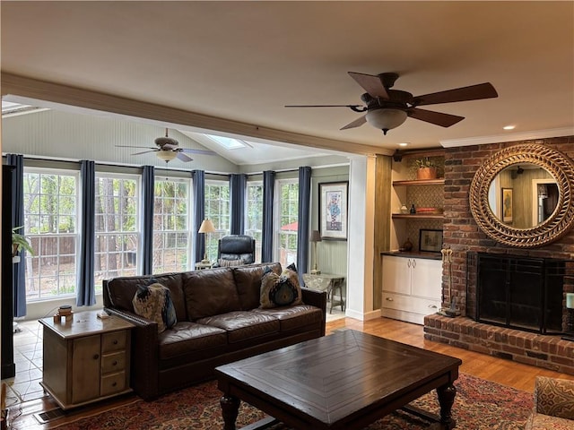 living area with ceiling fan, a skylight, crown molding, wood finished floors, and a brick fireplace