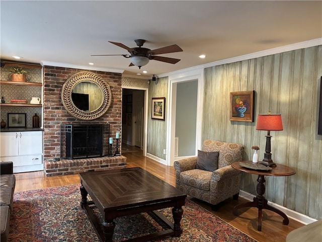 living room with a ceiling fan, crown molding, wood finished floors, a brick fireplace, and baseboards