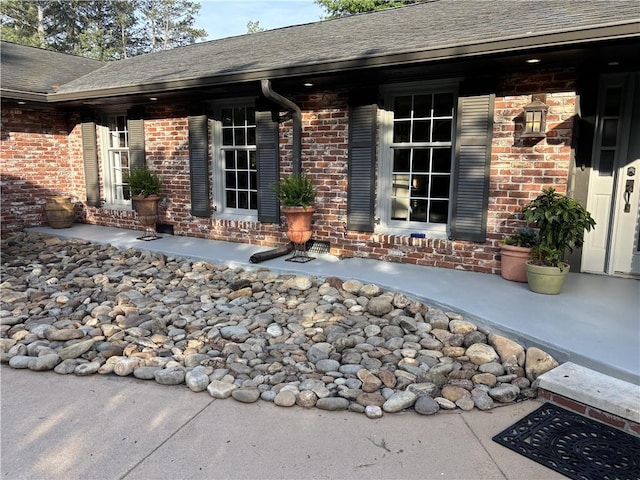 view of exterior entry featuring brick siding and a shingled roof