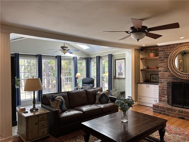 living area featuring ceiling fan, vaulted ceiling, a fireplace, wood finished floors, and a skylight