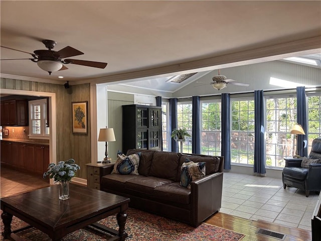 living area featuring a ceiling fan, lofted ceiling, light tile patterned floors, ornamental molding, and wood walls