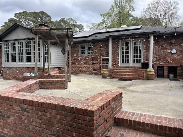 back of property with entry steps, solar panels, a chimney, and a patio area