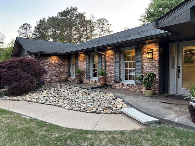 doorway to property featuring a shingled roof and brick siding