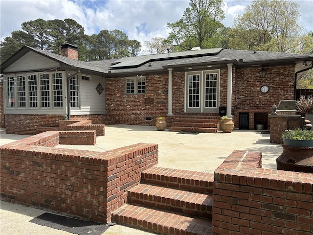 back of house with a chimney, brick siding, entry steps, and solar panels