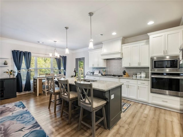 kitchen with premium range hood, white cabinets, stainless steel appliances, and hanging light fixtures