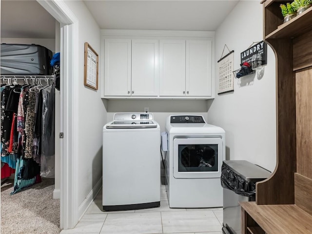 clothes washing area with washing machine and clothes dryer, light tile patterned floors, and cabinets