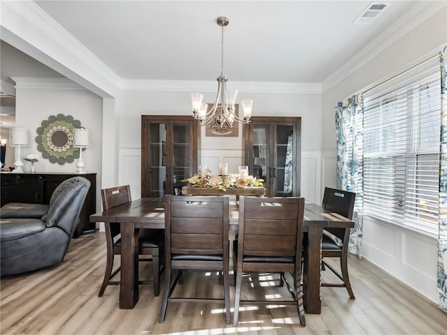 dining space with light hardwood / wood-style floors, crown molding, and an inviting chandelier