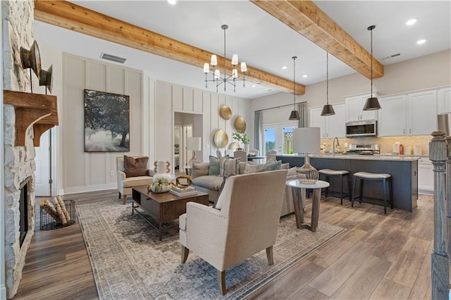 living room with dark hardwood / wood-style floors, a fireplace, sink, a chandelier, and beam ceiling