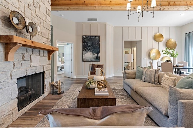 living room with a notable chandelier, dark wood-type flooring, a fireplace, and beamed ceiling