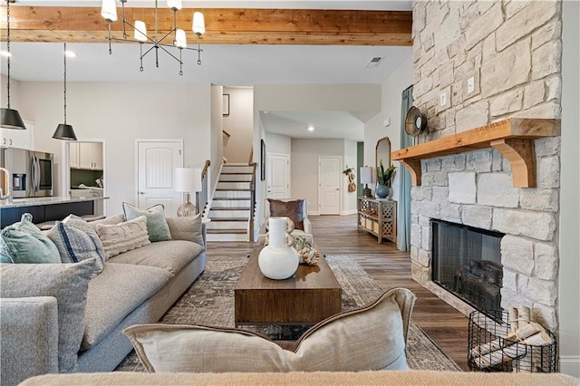 living room featuring dark wood-type flooring, a towering ceiling, a notable chandelier, a stone fireplace, and beamed ceiling