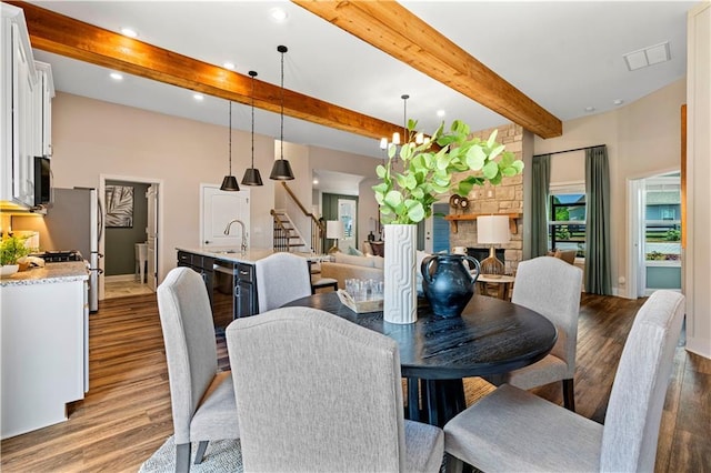 dining area featuring a stone fireplace, sink, a notable chandelier, beamed ceiling, and light hardwood / wood-style floors