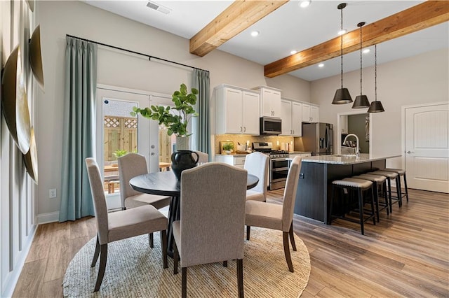 dining area featuring beam ceiling, sink, and light hardwood / wood-style flooring