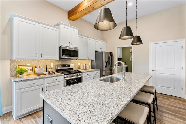 kitchen with white cabinetry, stainless steel appliances, sink, and a kitchen island with sink