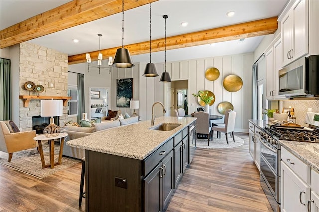 kitchen featuring sink, appliances with stainless steel finishes, white cabinetry, an island with sink, and decorative light fixtures