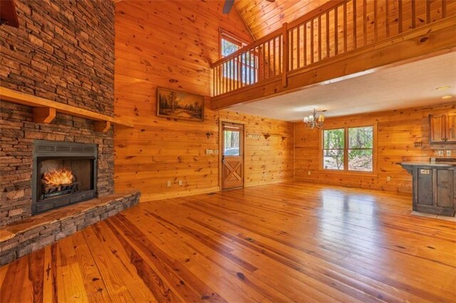 342 Zenith Trl, Ellijay, GA 30540 - unfurnished living room with a notable chandelier, wood walls, a stone fireplace, wood-type flooring, and high vaulted ceiling