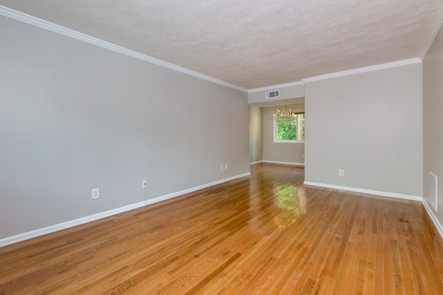 empty room with a notable chandelier, a textured ceiling, baseboards, visible vents, and light wood-style floors