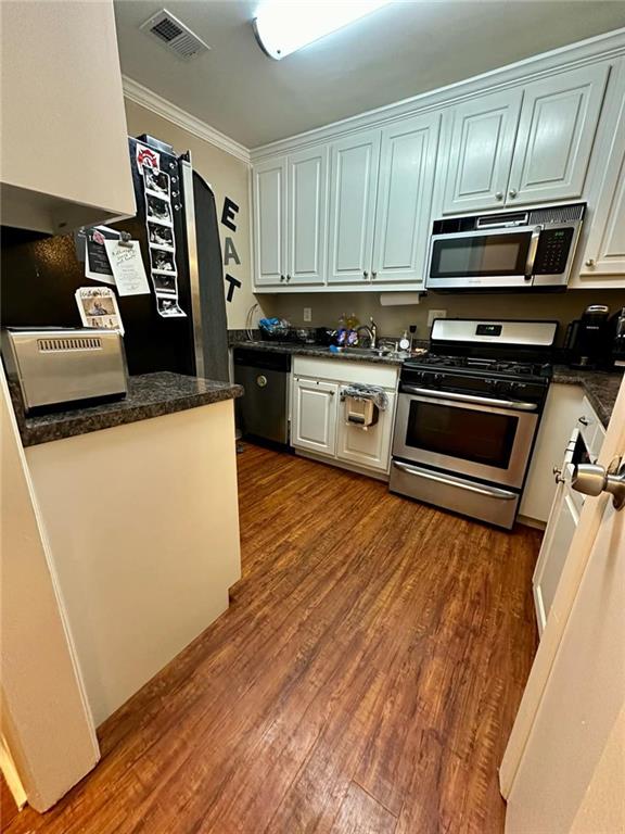 kitchen with white cabinetry, dark hardwood / wood-style flooring, ornamental molding, and appliances with stainless steel finishes