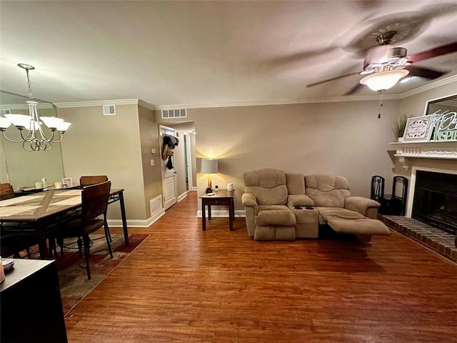 living room with crown molding, a fireplace, hardwood / wood-style floors, and ceiling fan with notable chandelier