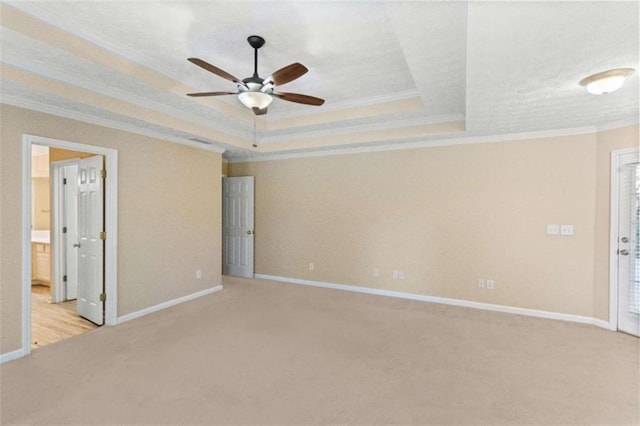 carpeted empty room with a tray ceiling, ceiling fan, and ornamental molding