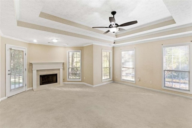 unfurnished living room featuring ornamental molding, a tray ceiling, light colored carpet, ceiling fan, and a fireplace