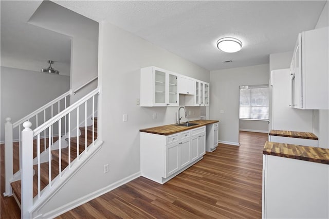 kitchen with dark wood finished floors, butcher block counters, glass insert cabinets, white cabinetry, and a sink