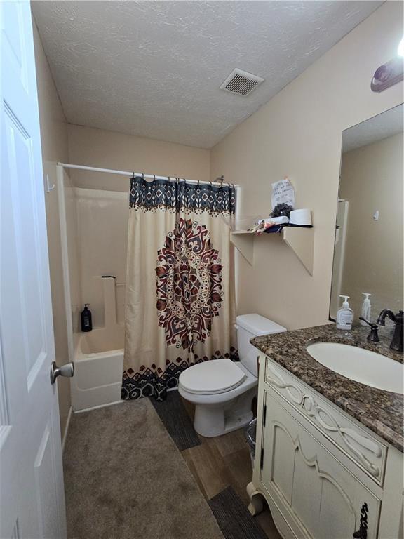 bathroom featuring visible vents, toilet, shower / bath combo with shower curtain, a textured ceiling, and vanity