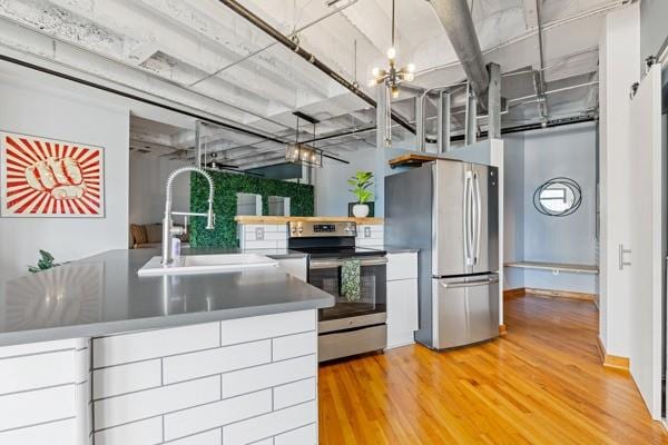 kitchen featuring wood-type flooring, sink, a notable chandelier, a barn door, and stainless steel appliances