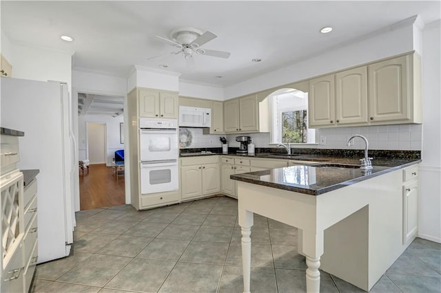 kitchen with white appliances, decorative backsplash, kitchen peninsula, light tile patterned floors, and dark stone countertops