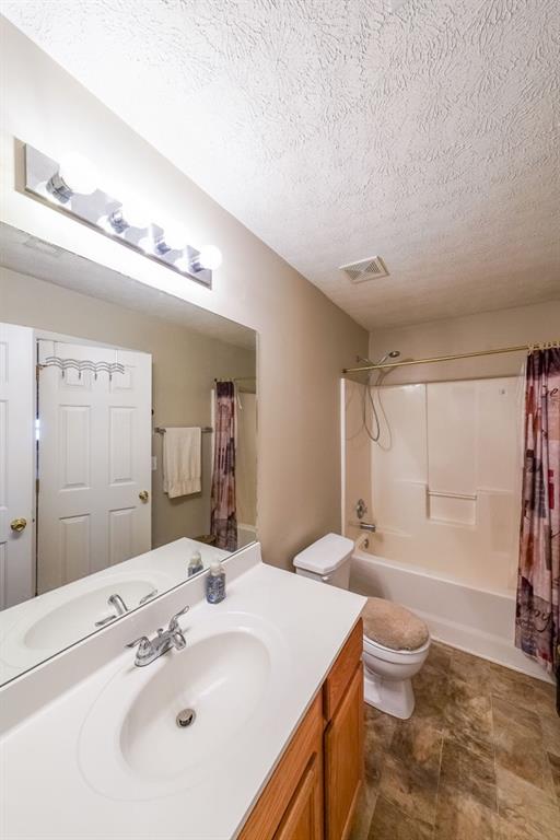 full bathroom featuring toilet, a textured ceiling, vanity, and shower / tub combo