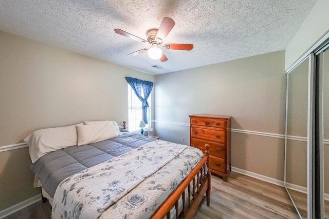 bedroom featuring light hardwood / wood-style flooring, a textured ceiling, a closet, and ceiling fan