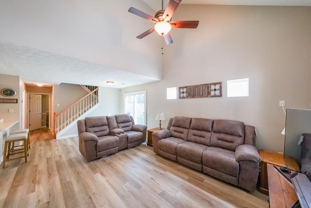 living room featuring light hardwood / wood-style flooring, a textured ceiling, high vaulted ceiling, and ceiling fan