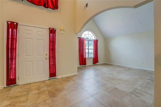 entryway featuring lofted ceiling, arched walkways, visible vents, baseboards, and tile patterned floors