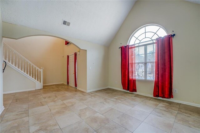 unfurnished room with arched walkways, lofted ceiling, visible vents, baseboards, and stairs