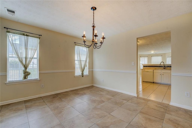 empty room featuring a notable chandelier, visible vents, a sink, a textured ceiling, and baseboards