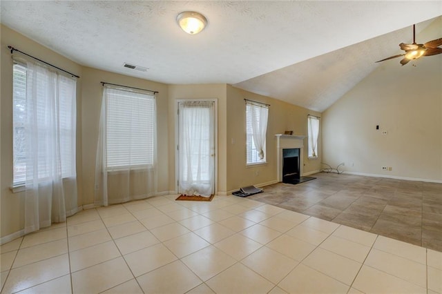 unfurnished living room with visible vents, a fireplace with raised hearth, tile patterned flooring, vaulted ceiling, and a textured ceiling