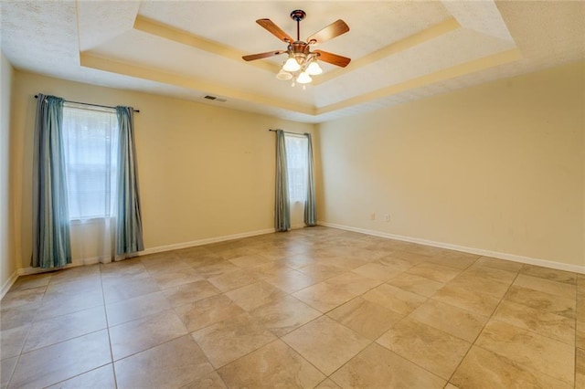 empty room with plenty of natural light, a tray ceiling, and baseboards