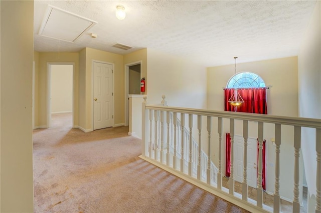 hallway with a textured ceiling, visible vents, baseboards, carpet, and attic access